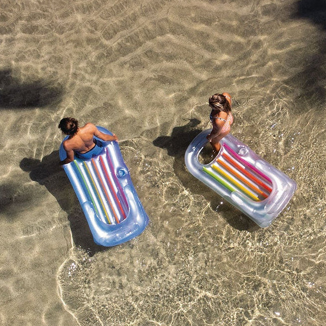 This is a lifestyle image showing two people bringing their inflatable chairs out of the ocean onto the beach.