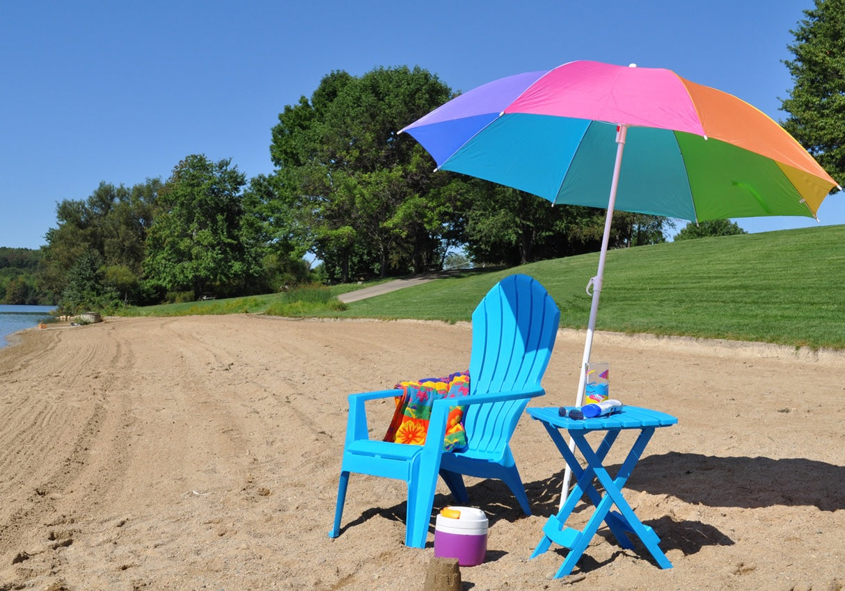 A pool blue colored Adirondack chair underneath a rainbow umbrella on the beach.