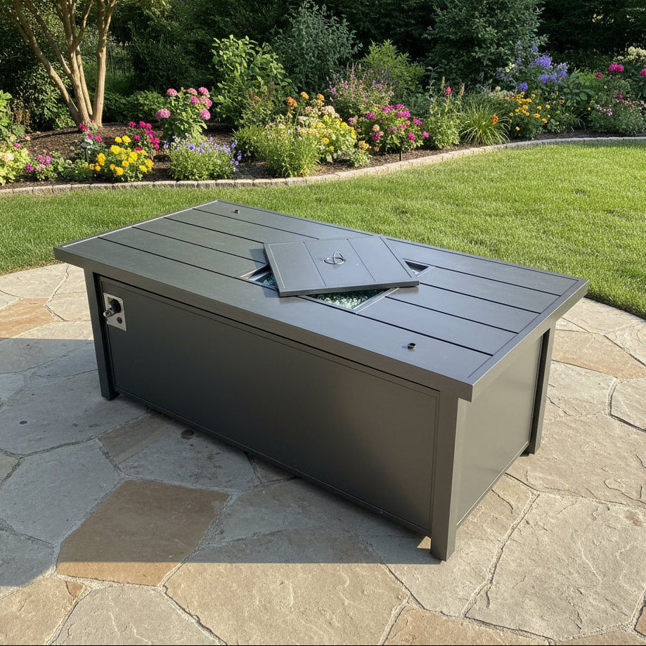 This is a lifestyle image showing what this fire pit table looks like on a stone patio in a grassy backyard.
