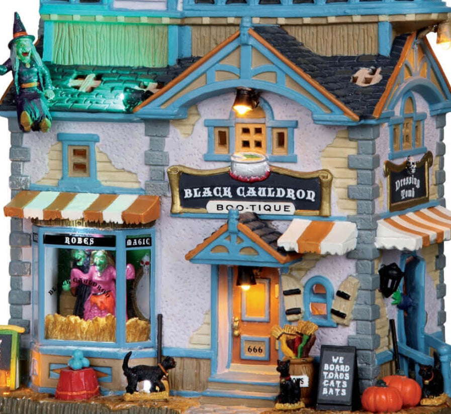 Porcelain lighted building for a Lemax display. Designed to look like a boutique store. There are witches, gargoyles, pumpkins and black cats. Inside the window, you can see a monster trying on a pink dress.