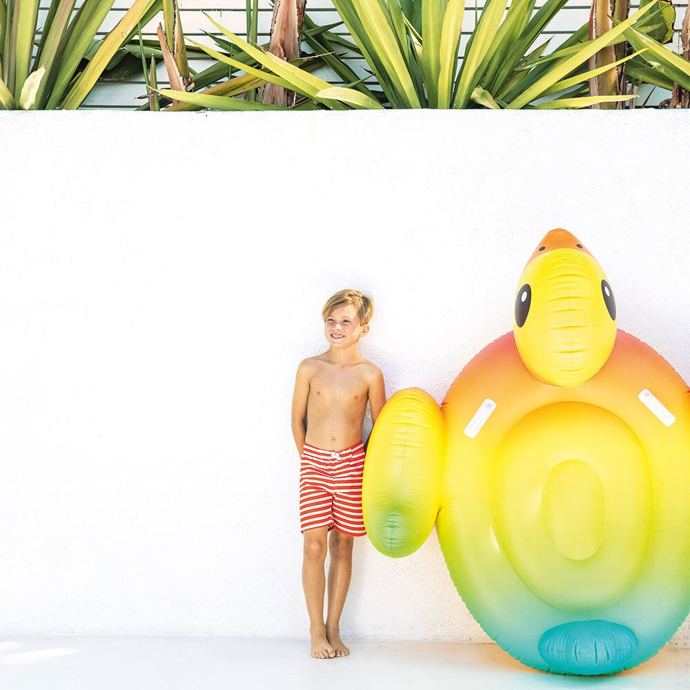 This is a lifestyle image showing a young boy standing up against a white wall while the inflatable duck rests alongside him.
