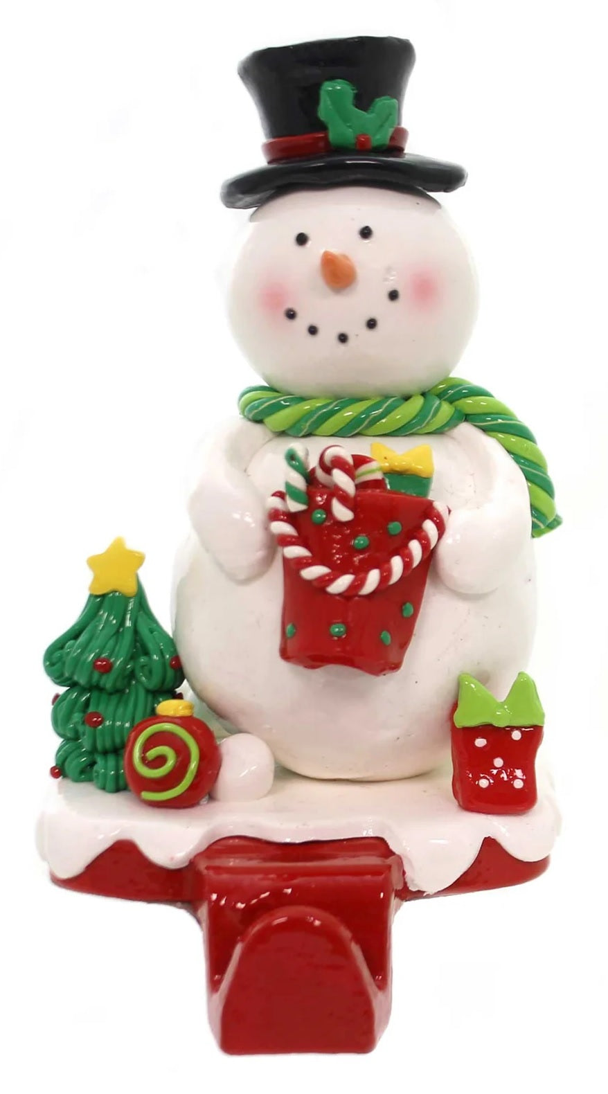 Stocking holder with a Snowman on it. He's holding a basket and is standing next to a small decorated Christmas tree, an ornament and a gift.