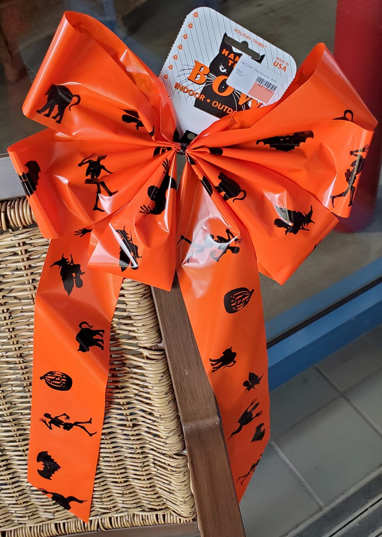 Orange bow with black figures on it. The figures include a skeleton, a pumpkin, a cat, a switch on a broom and a bat.