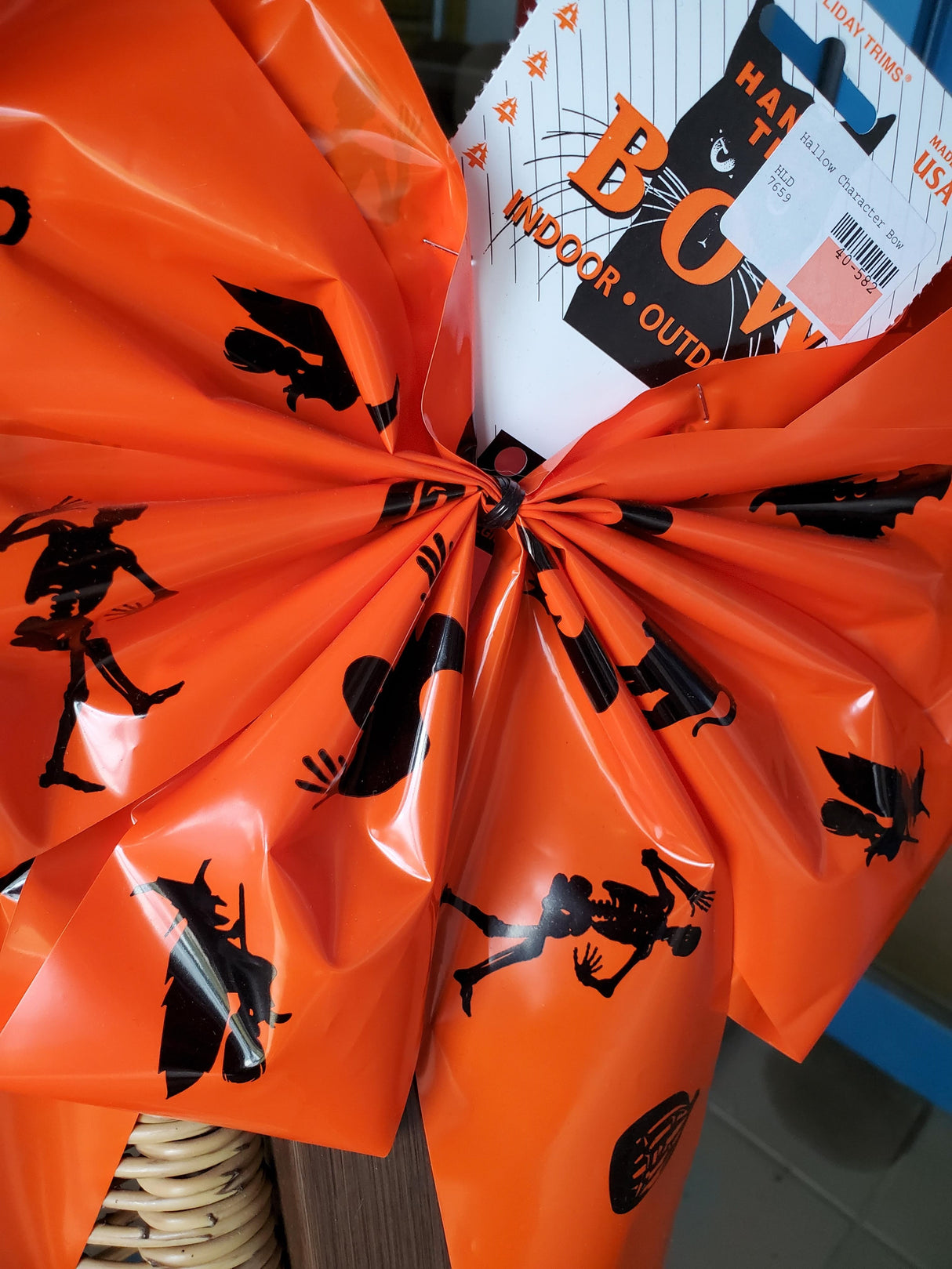 Orange bow with black figures on it. The figures include a skeleton, a pumpkin, a cat, a switch on a broom and a bat.