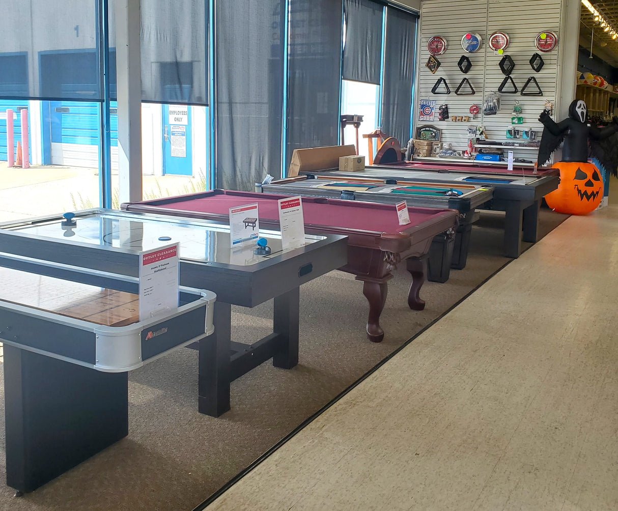 Clearance display of a shuffleboard, air hockey table, and billiard tables at the Tinley Park Outlet store.