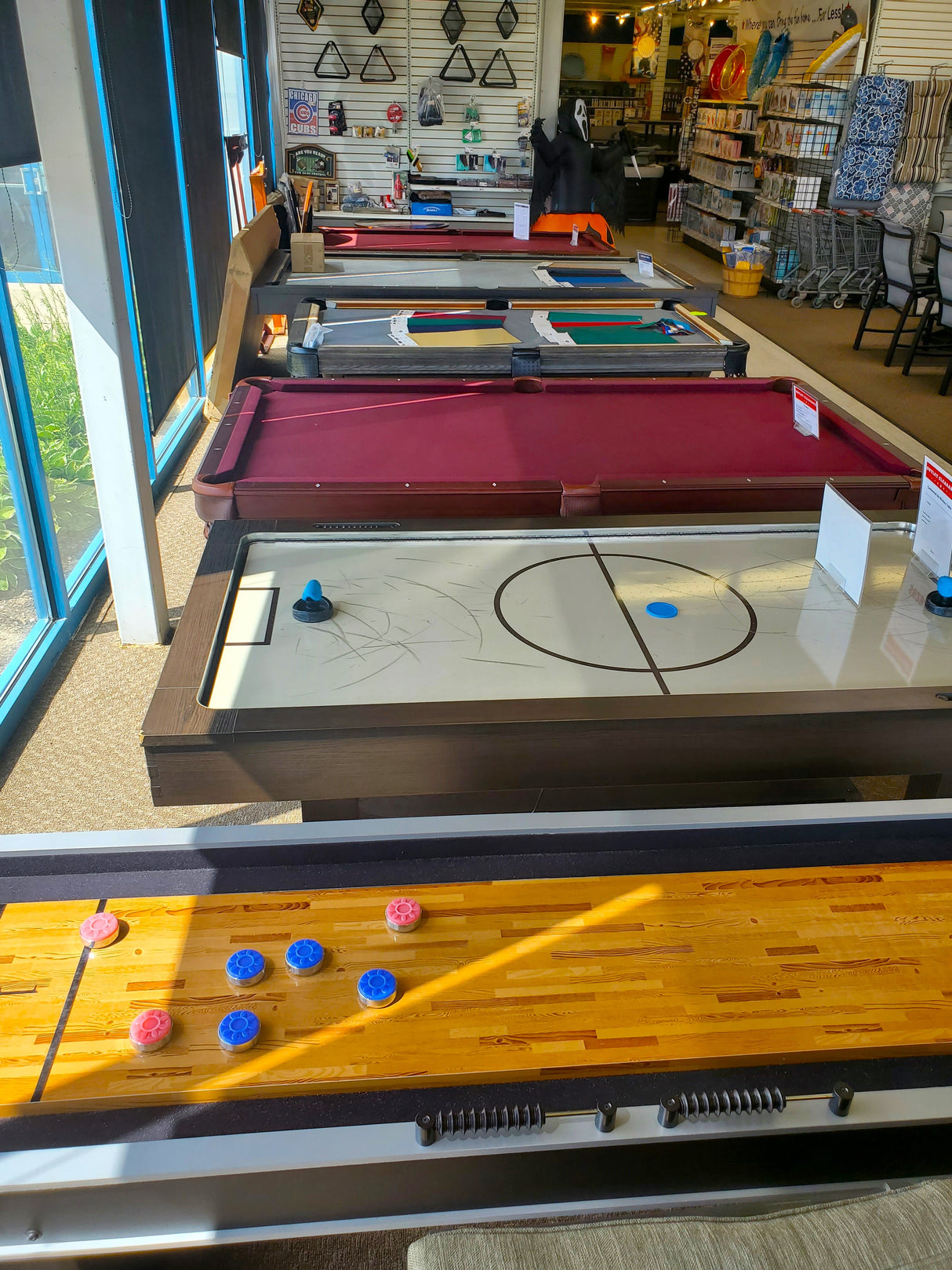 In store display of clearance game tables. A shuffleboard table, air hockey table, and various billiard tables for sale at the Tinley Park Outlet store.