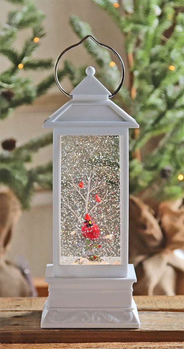 White lantern decoration with glitter and a woodland scene with a cardinal inside.