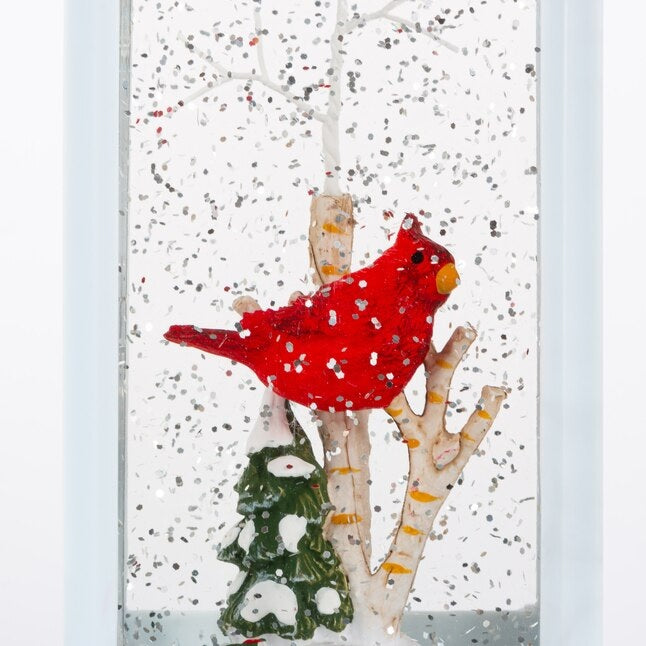 White lantern decoration with glitter and a woodland scene with a cardinal inside.