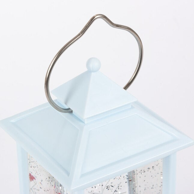 White lantern decoration with glitter and a woodland scene with a cardinal inside.