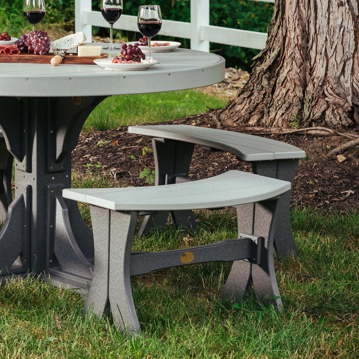 This is the Dove Gray and Black colored Table Bench in front of a matching table in a grassy backyard. On the table are plates and wine glasses and a charcuterie board of meats, cheeses and grapes.