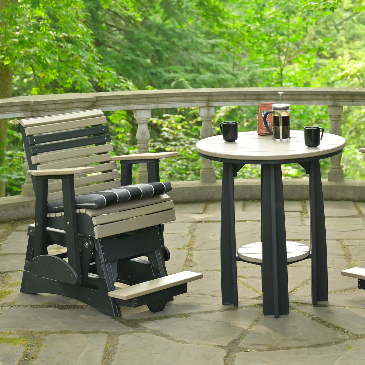 This is a lifestyle image showing the Weatherwood and Black colored glider chair on a stone patio next to a matching table.