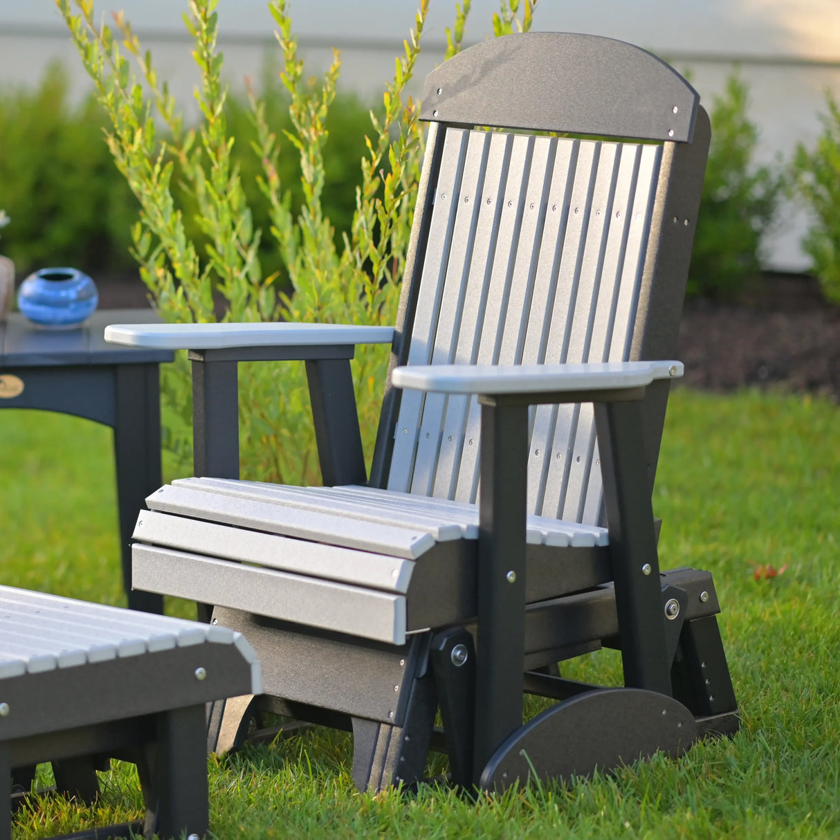 This is a lifestyle image showing the Dove Gray and Black colored classic glider chair in a grassy yard.