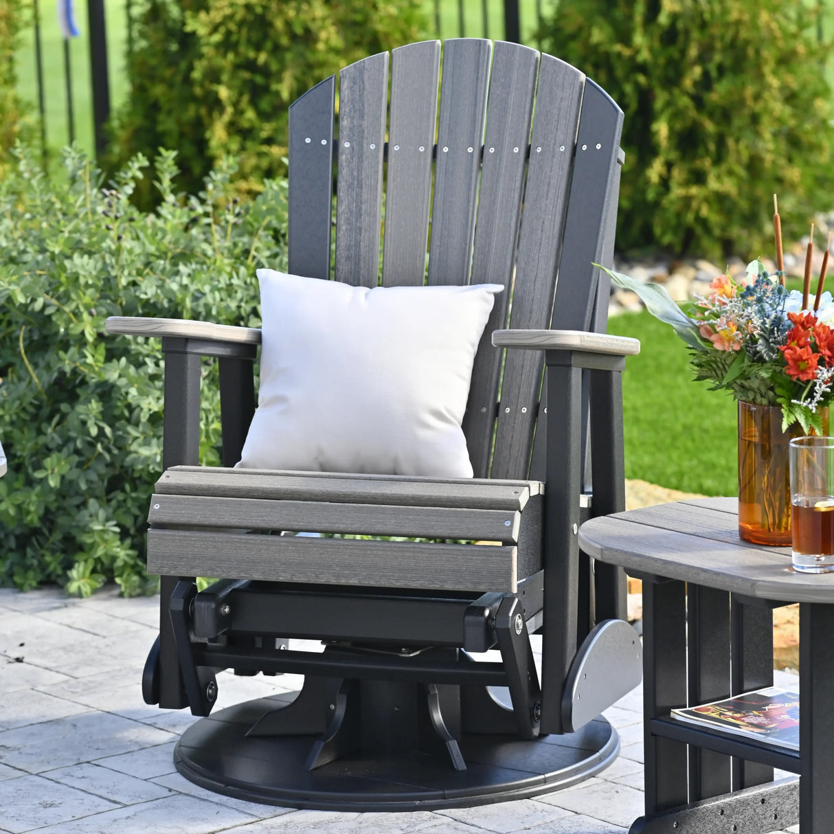 This is a lifestyle image showing the Dove Gray and Black colored Adirondack swivel glider chair on a stone patio.
