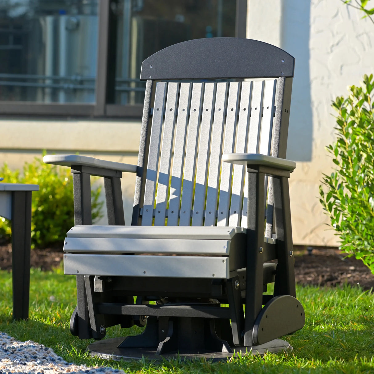 This is a lifestyle image showing the Dove Gray and Black colored swivel glider chair in a grassy yard.