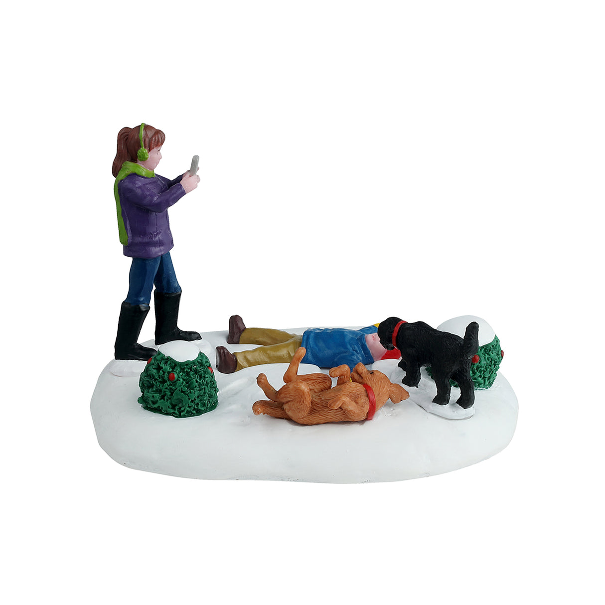 Resin table accent for a Lemax Village tabletop display. Designed to look like a young child making a snow angel while a girl takes a picture of the scene. There are two dogs and two bushes nearby. One dog is black and one is a golden brown color. The golden brown dog is laying on it's back with it's tongue hanging out. The ground is covered in snow and both kids are wearing winter clothes.