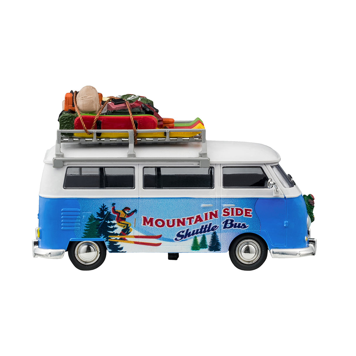 Plastic table accent for a Lemax display. Designed to look like a blue and white Volkswagen shuttle bus. The sides of the bus read "Mountain Side Shuttle Bus" and features a mural of someone skiing down a snowy hill surrounded by trees. There's a wreath on the front bumper. There's a ladder on the side leading up to the roof o the bus that's holding a bunch of ski equipment and luggage.