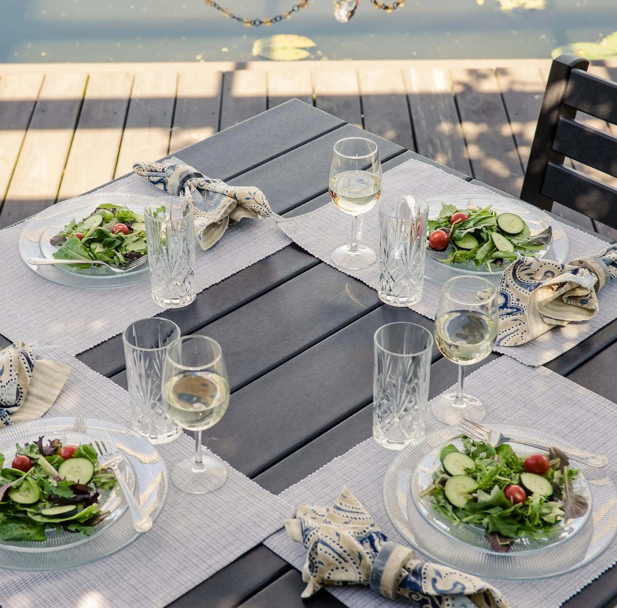 This is an up close view at the Black colored table that has four dinner mats, four sets of plates, four sets of wine glasses and four sets of water glasses. There's a salad on every plate.