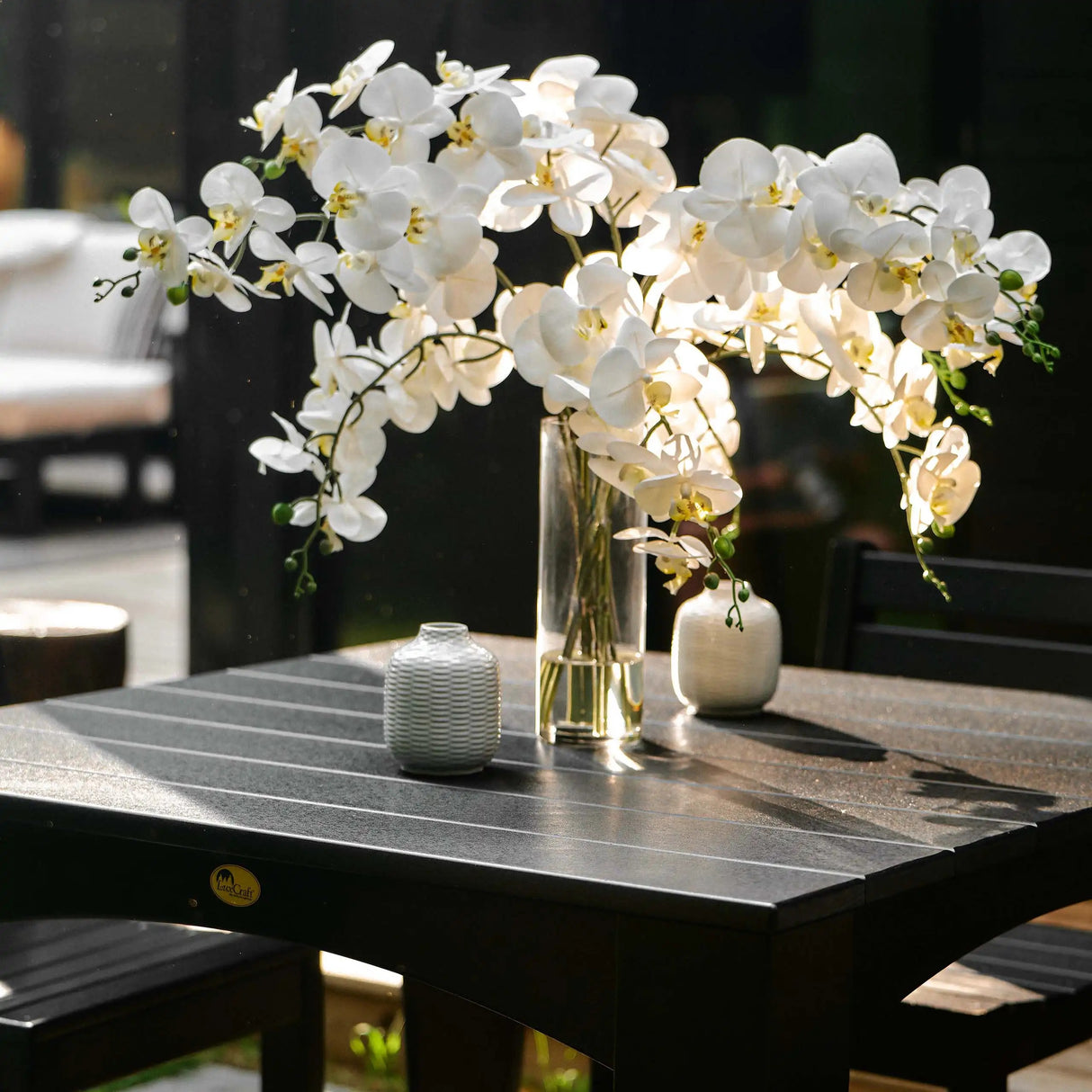 This is an up close view of the Black colored square dining table. There's a vase on the table filled with orchids.