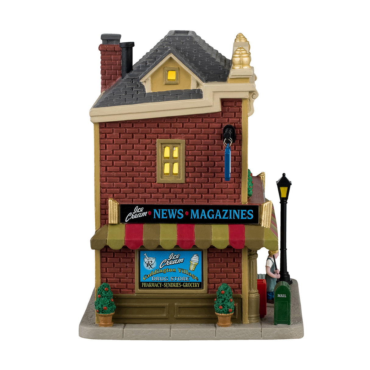 Porcelain lighted building for a Lemax display. Designed to look like a Village Drug Store. Established 1918, there's a pharmacy, sundries, groceries and ice cream. There's a mail box, a cooler with pop, a bench, a gumball machine and potted trees on the sidewalk.