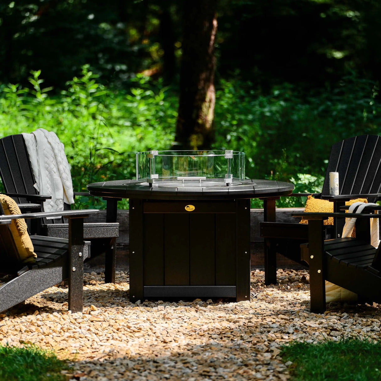 This is a lifestyle image showing the Black colored fire pit table surrounded by Black colored Adirondack chairs.