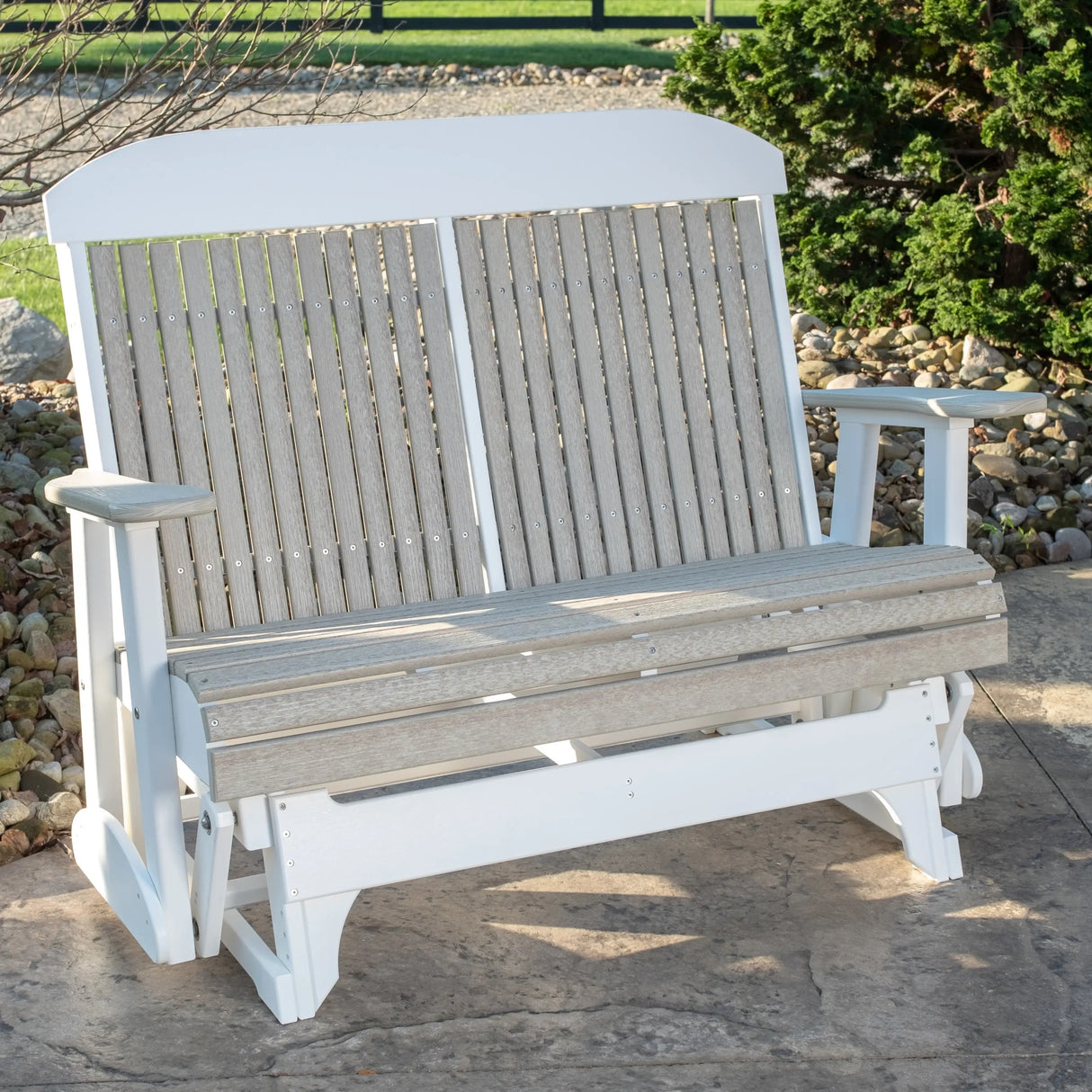 This is a lifestyle image showing the Birch and White colored classic glider bench on a stone patio.