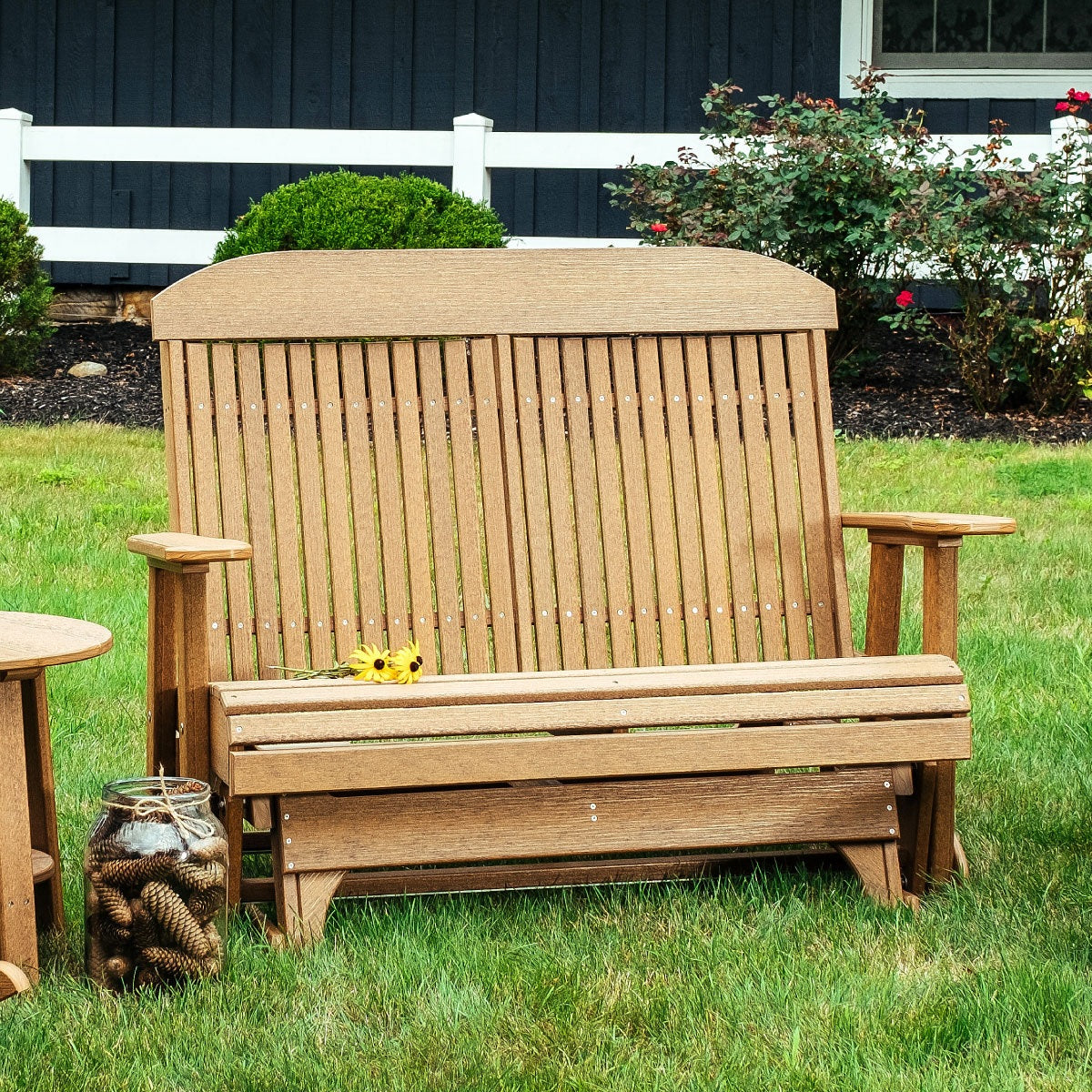 This is a lifestyle image showing the Antique Mahogany colored classic glider bench in a grassy backyard.