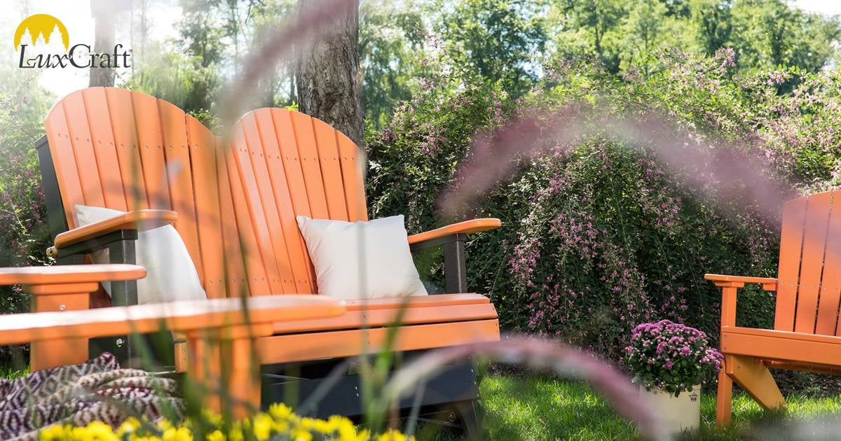 This is a lifestyle image showing the Tangerine and Black colored Adirondack glider bench in a grassy backyard, taken from underneath.