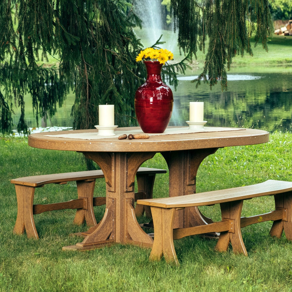 This is a lifestyle image showing the Antique Mahogany colored oval table with matching benches. This dining set is near a little pond in a grassy backyard.
