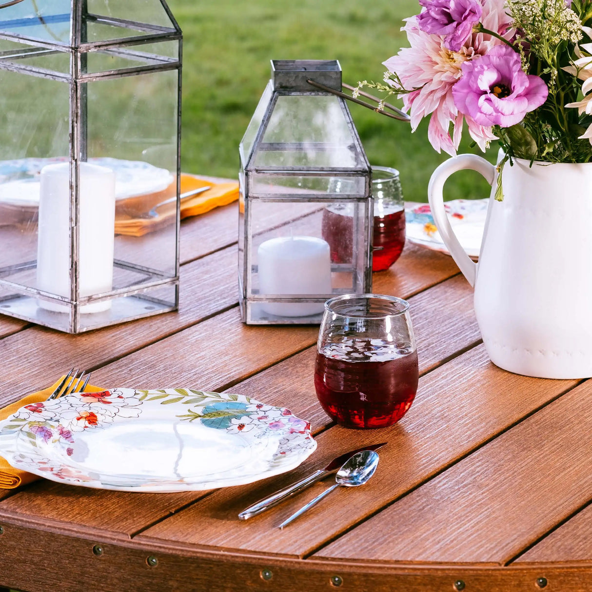 This is an up close view of the Antique Mahogany colored table. On the table, there are two candles, two glasses of wine, two plates and a vase with pretty flowers.