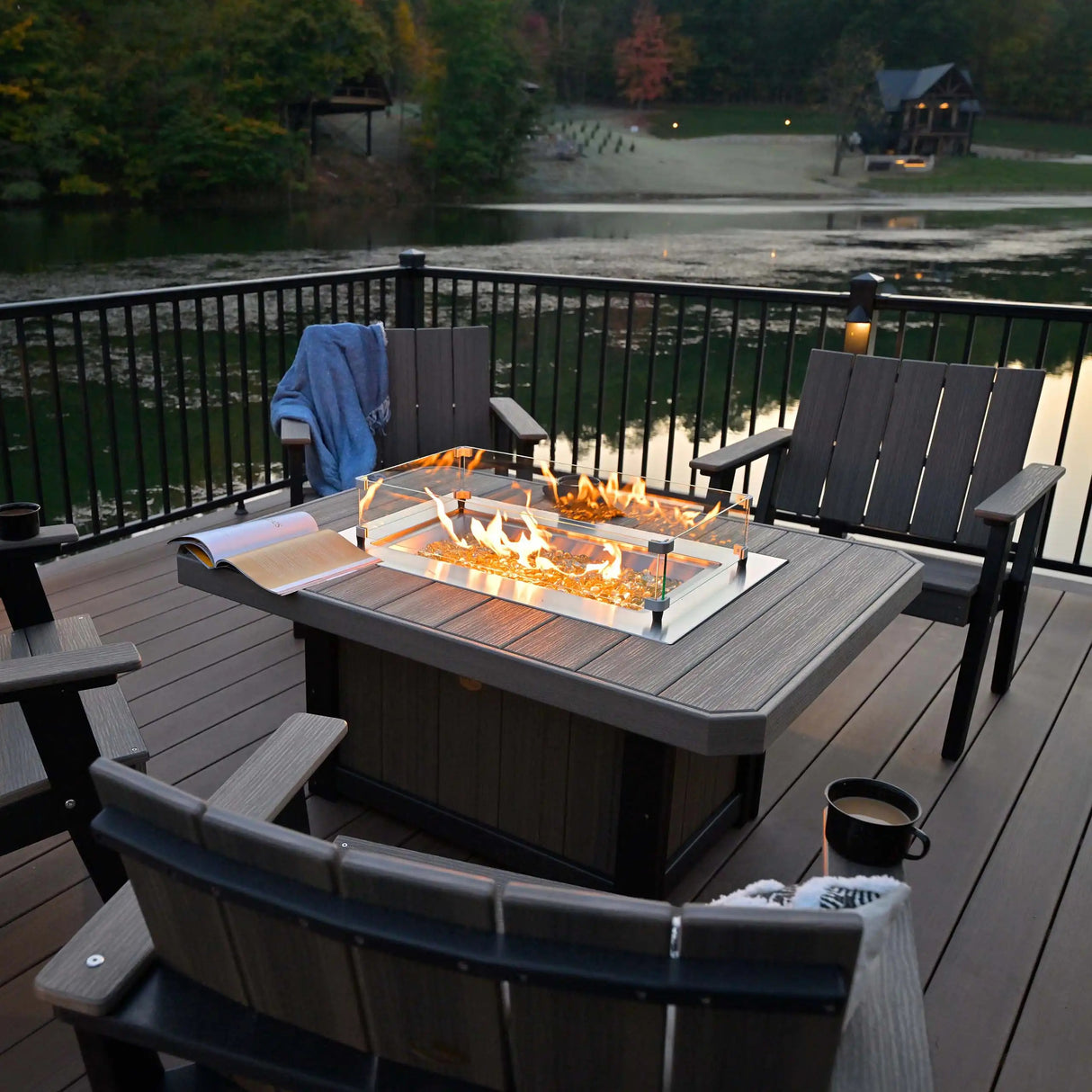 This is a lifestyle image showing the Coastal Gray and Black colored rectangular fire pit table near a body of water.