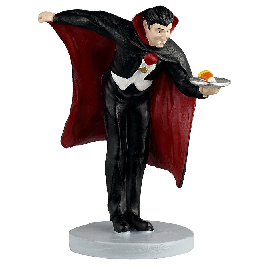 This image shows what this Lemax Spooky Town figurine looks like on a white background. It was designed to look like a vampire wearing a black and white tuxedo with a red and black cape. He's holding a silver plate with a piece of candy corn on it.