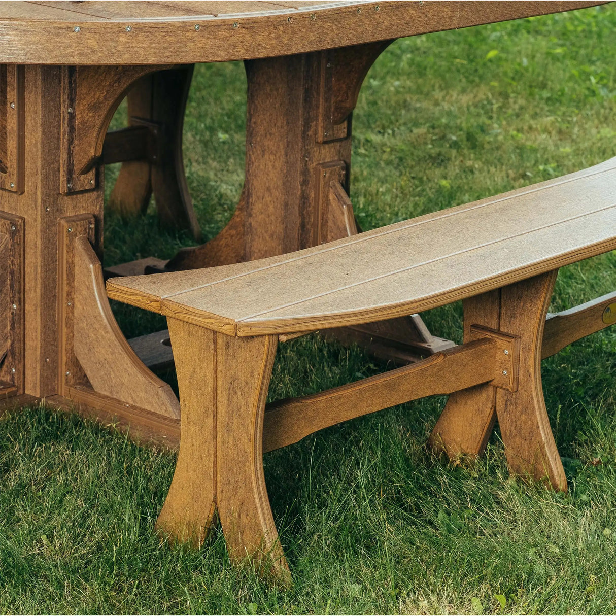 This is a lifestyle image showing the Antique Mahogany colored Table Bench around a matching table in a grassy backyard.