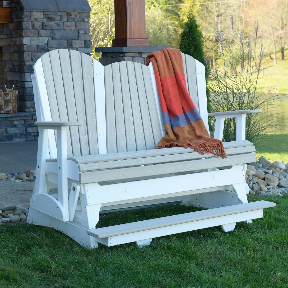 This is a lifestyle image of a Birch and White Adirondack balcony glider bench with an orange and pink blanket draped over the side.