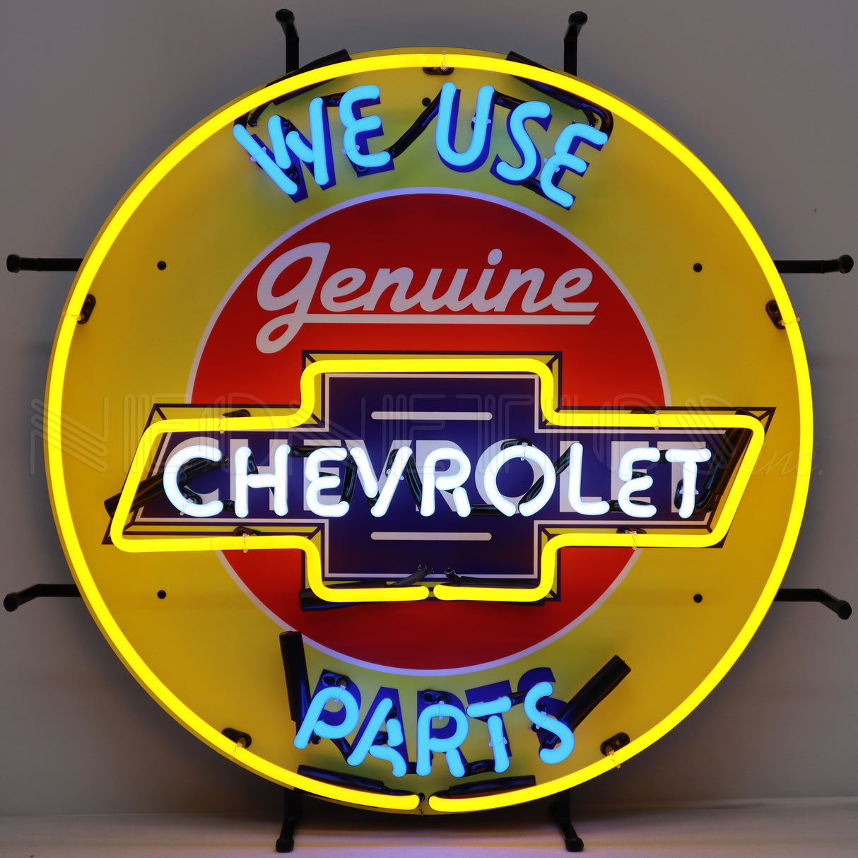 This particular image shows this neon sign with lights on. Circular neon sign that reads "We use genuine Chevrolet parts." The background is yellow and the texts are all different colors: Light blue, red, white and dark blue.
