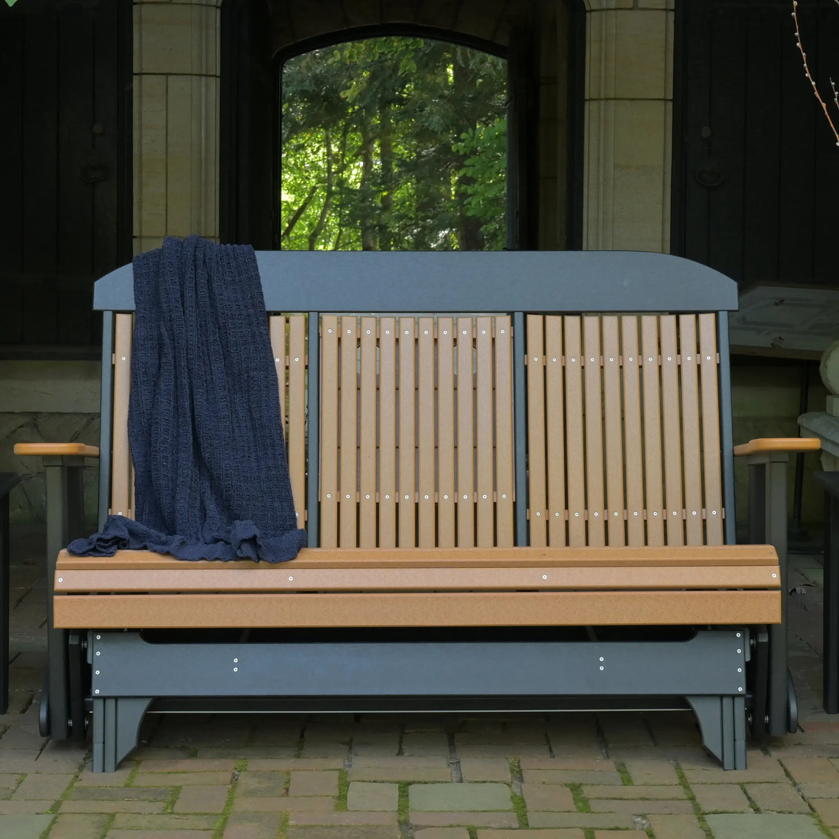 This is a lifestyle image showing the Cedar and Black colored classic glider bench in front of a house.