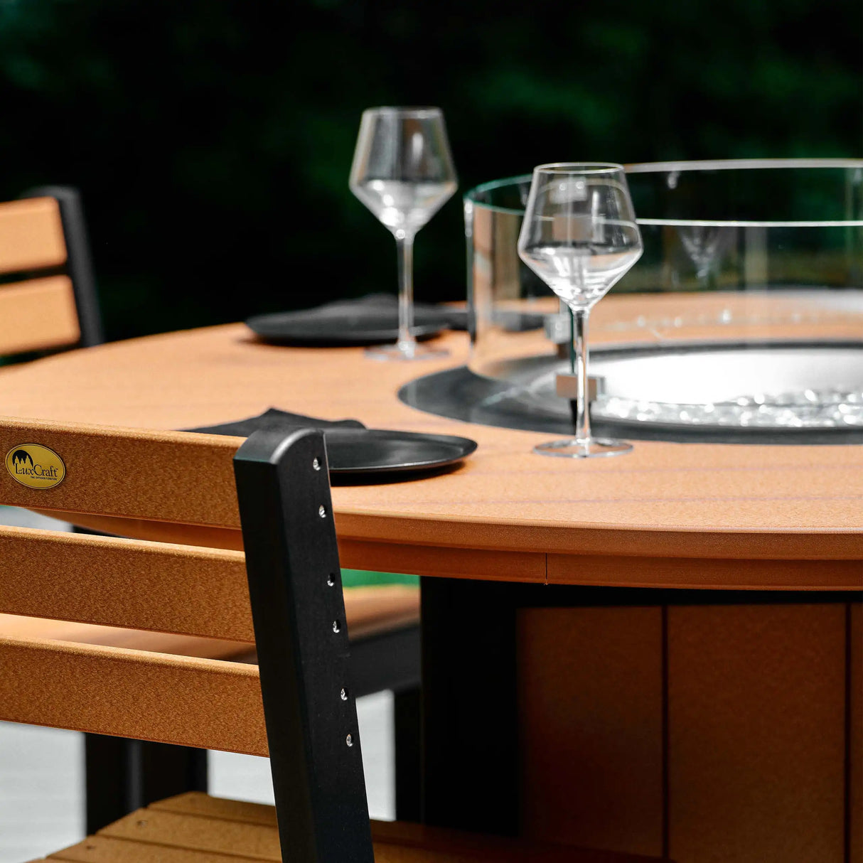 This is a lifestyle image showing the Cedar and Black colored fire table up close. There are plates and silverware and wine glasses on the table.