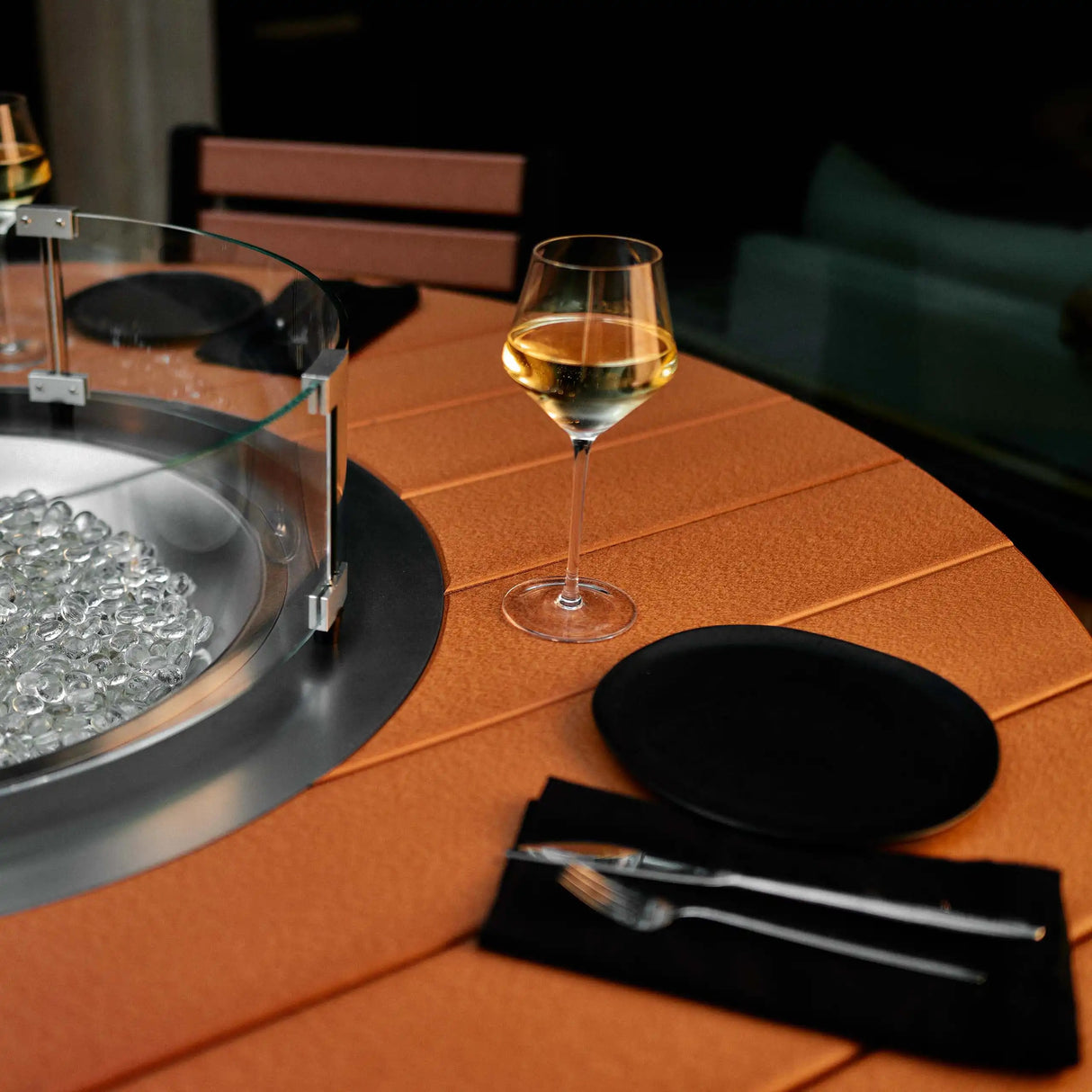 This is a lifestyle image showing the Cedar and Black colored fire table up close. There are plates and silverware and wine glasses on the table.