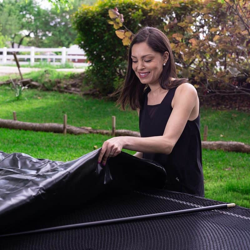 This is a lifestyle image showing a woman putting the cover on her trampoline.