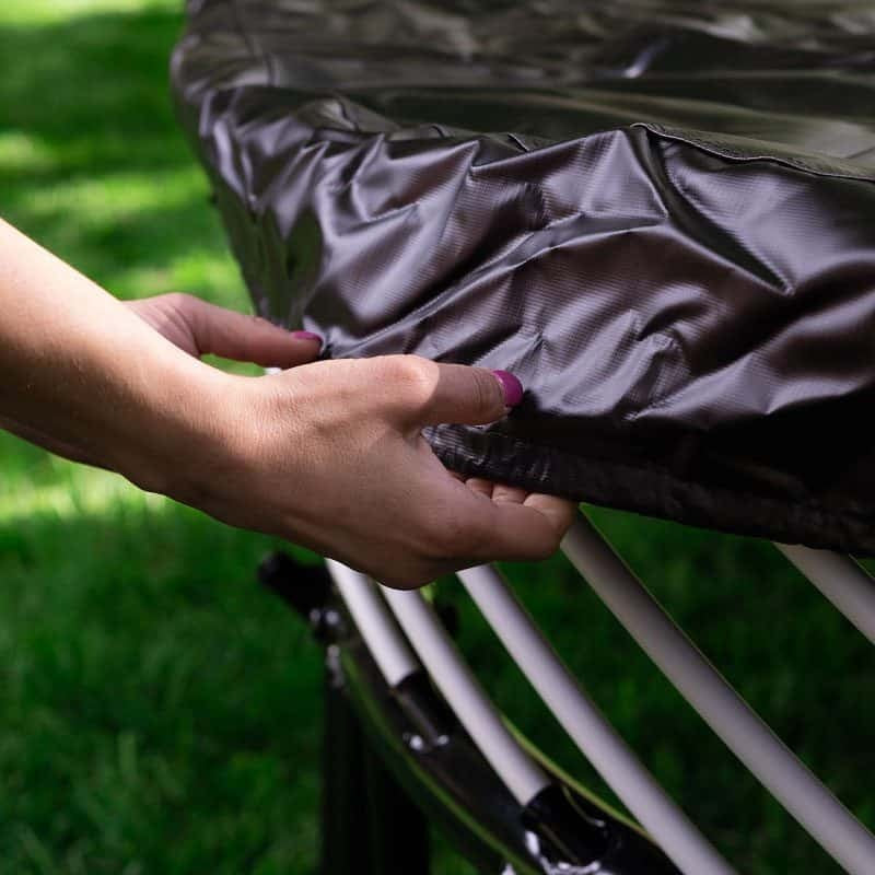 This is an up close image of someone's hands pulling the cover over the edge of a trampoline.