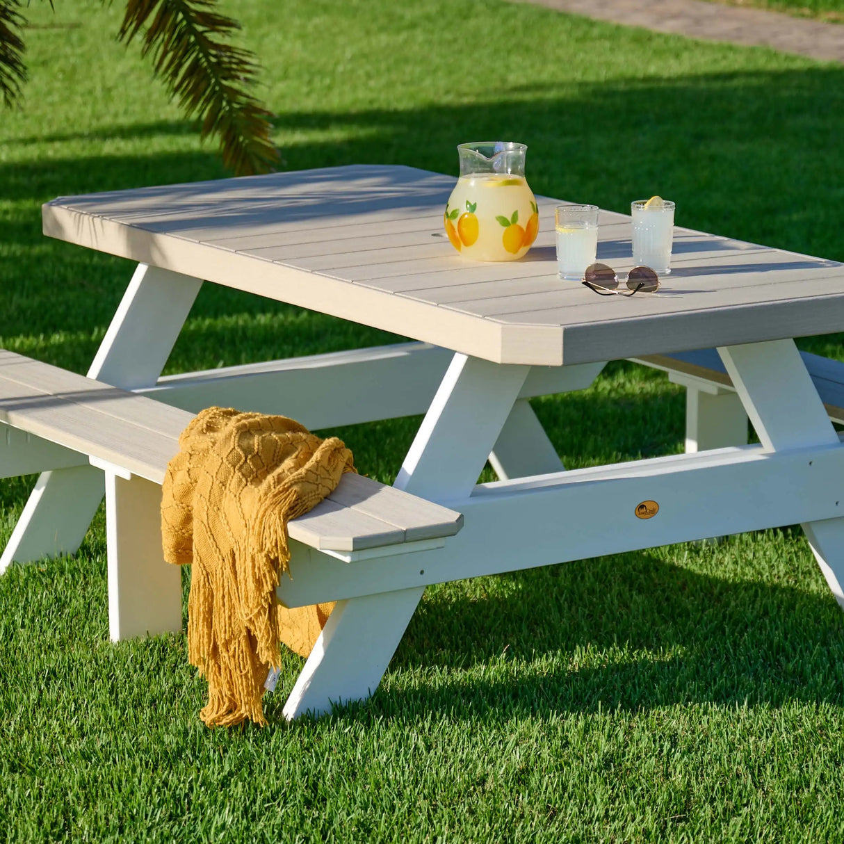 This is a lifestyle image showing the Birch and White colored picnic table with attached benches. There's a yellow blanket on one of the benches and a pitcher of lemonade on the table.