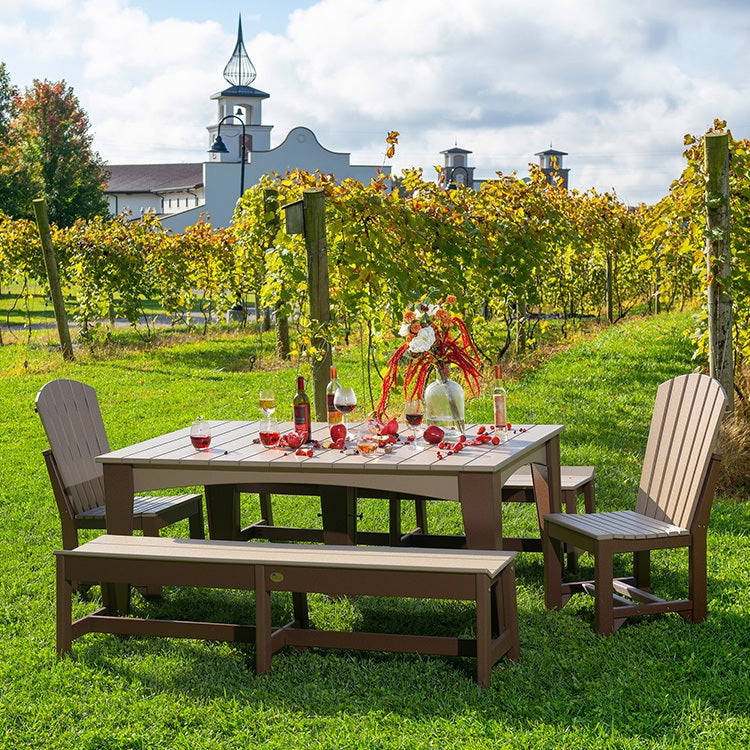 This is a lifestyle image showing the Weatherwood and Chestnut Brown colored rectangular dining table surrounded by matching chairs and benches. This patio dining set appears to be at the edge of a vineyard.