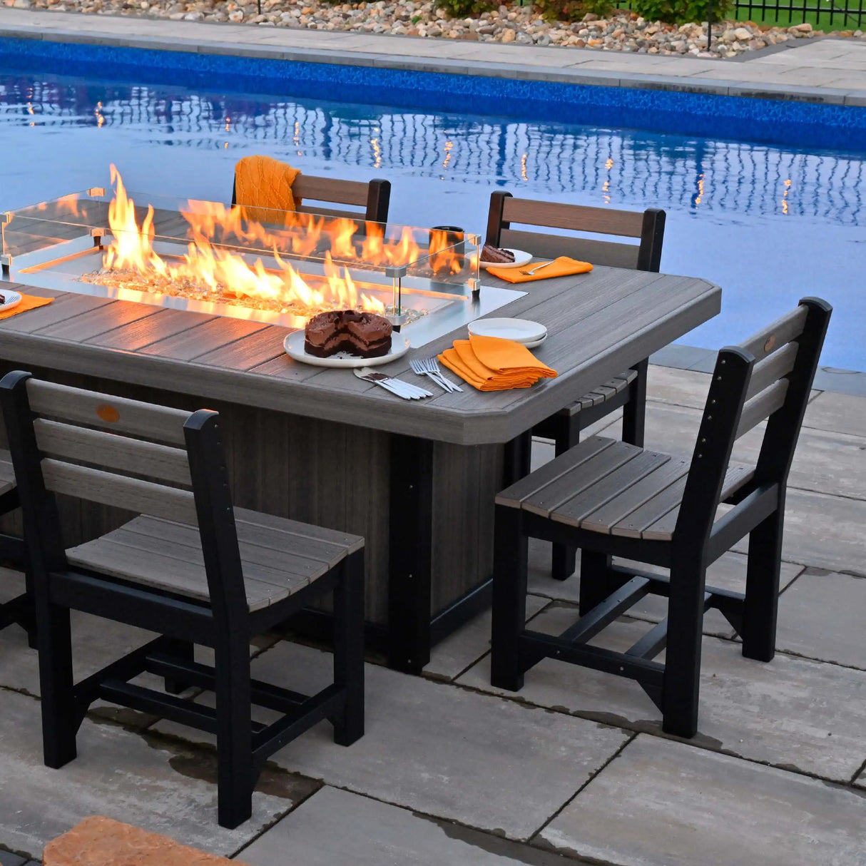 This is a lifestyle image showing the Dove Gray and Black colored fire pit table with matching chairs. They're next to a pool.