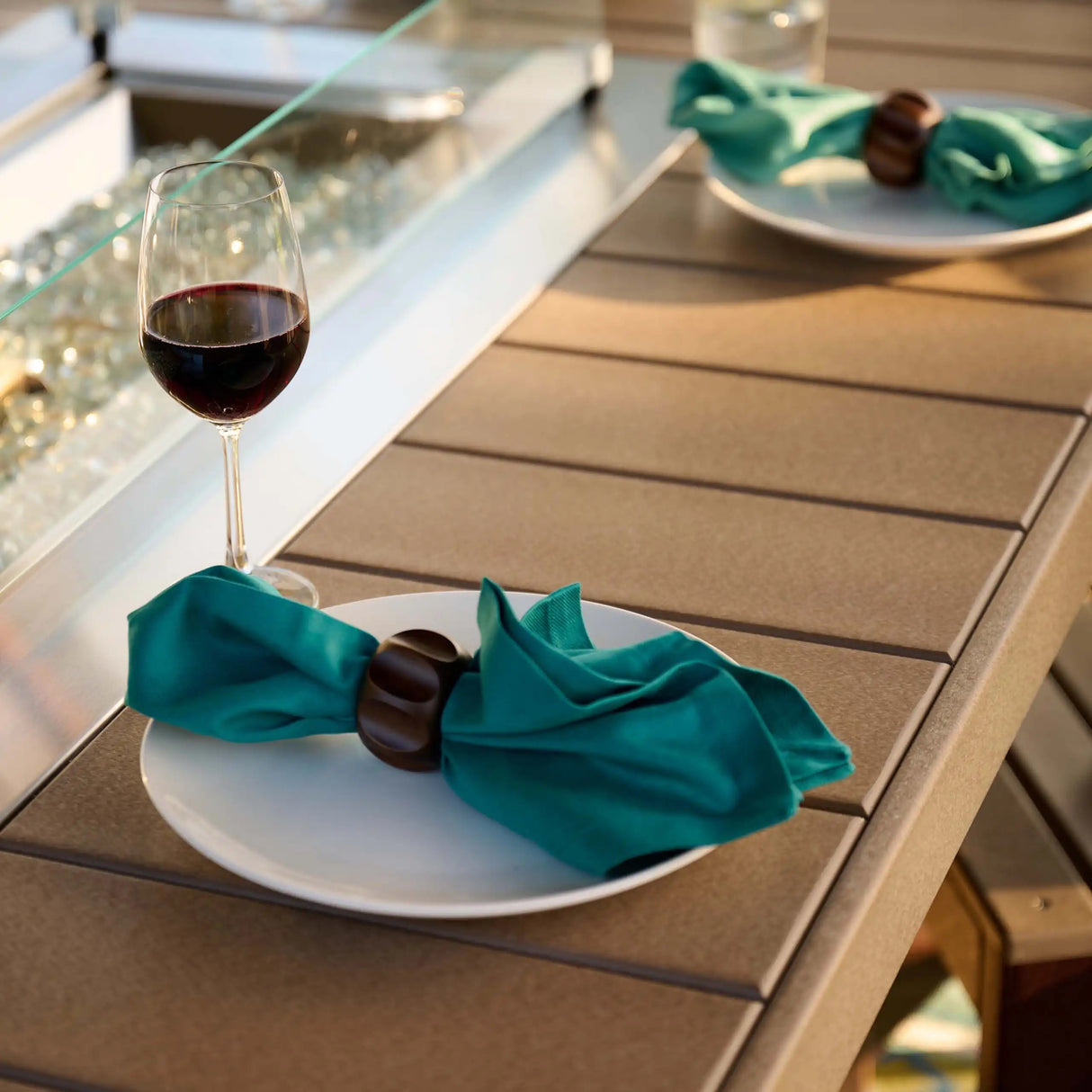 This is an up close view of the fire pit table. There are plates and napkins and wine glasses on it.