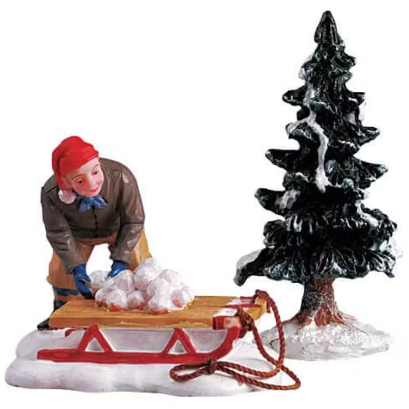Polyresin figurines for a Lemax display. Designed to look like a boy wearing winter clothes putting snowballs on a sled next to a snow-covered tree.