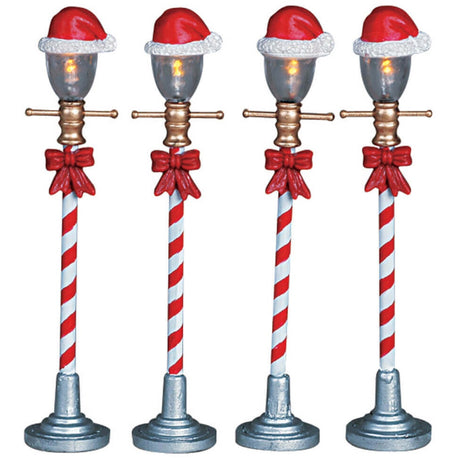 Village accents for a Lemax display. Designed to look like four lampposts. The poles look like red and white candy canes and there are Santa hats on top of the bulbs. Each lamp has a red bow tied to it.