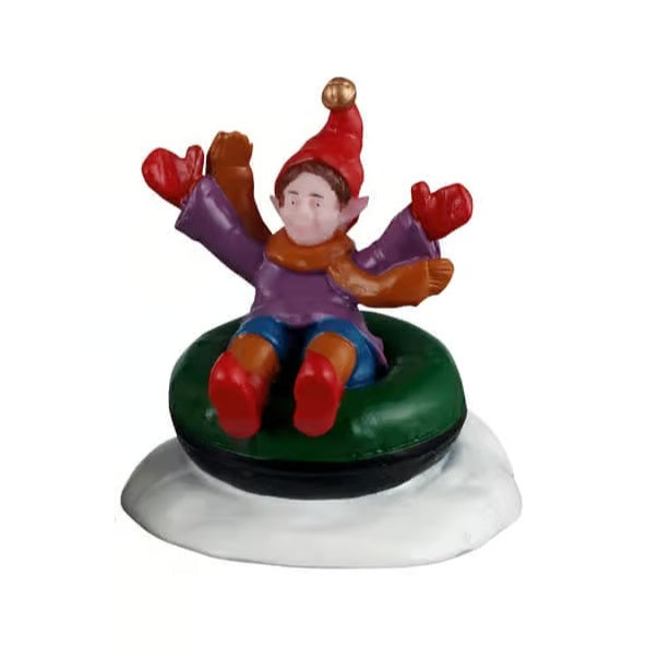 This figurine shows an elf in a green and black inner tube in the snow. The elf is wearing a red hat with a gold bell on the end. He's also wearing a brown scarf, a purple sweater, red gloves, blue and orange pants and red shoes.