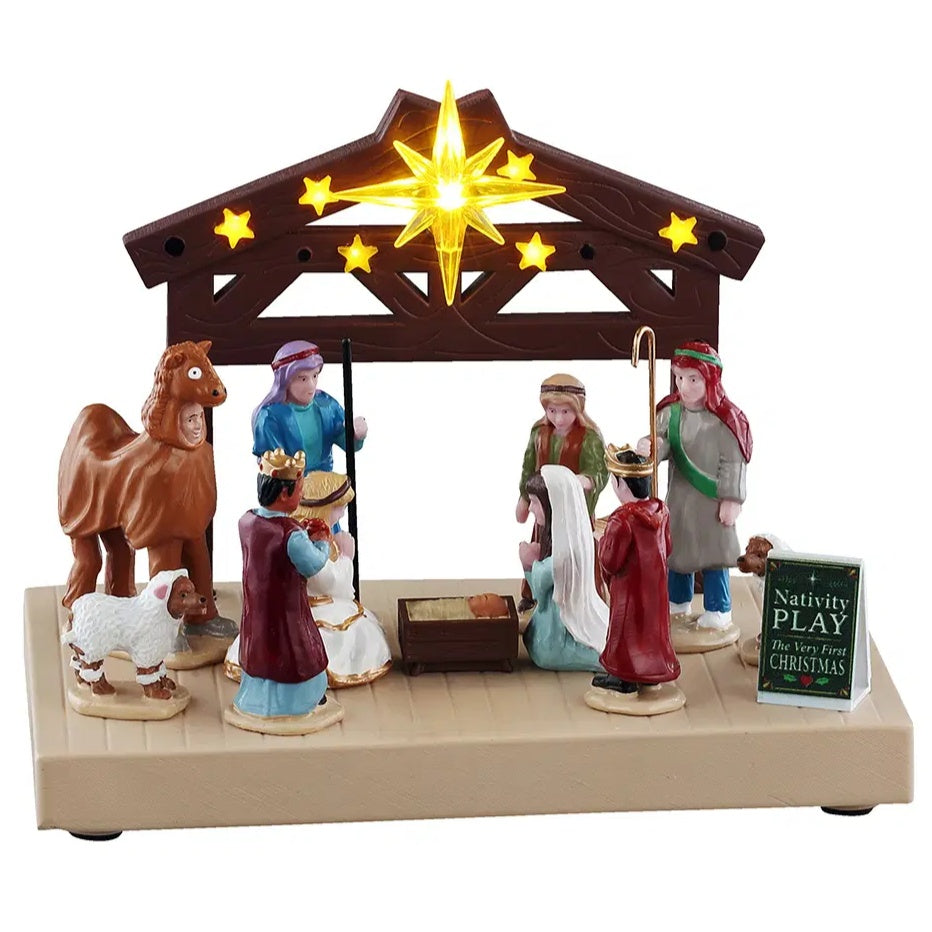 This image shows what this Lemax General Collectibles table accent looks like on a white background. It was designed to look like eight people putting on the Nativity play. They're on a wooden stage made to look like a barn decorated with lots of lit up stars.