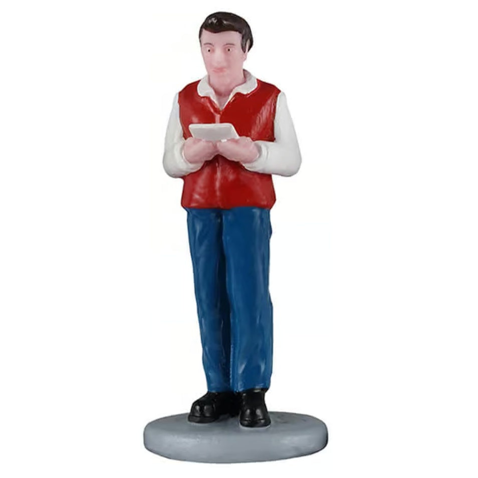 This image shows a man figurine holding a sheet of music and singing. He has brown hair and is wearing a white long sleeve shirt with a red vest, blue jeans and black shoes.