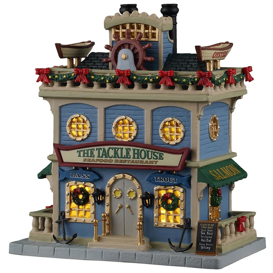 This image shows what this Lemax building looks like on a white background. It was designed to look like a tall seafood restaurant. On the roof, there are decorative boats and a steering wheel. The windows look like boat windows. On either side of the door, there are anchors. The building is also decorated with green garland, wreaths and red bows.