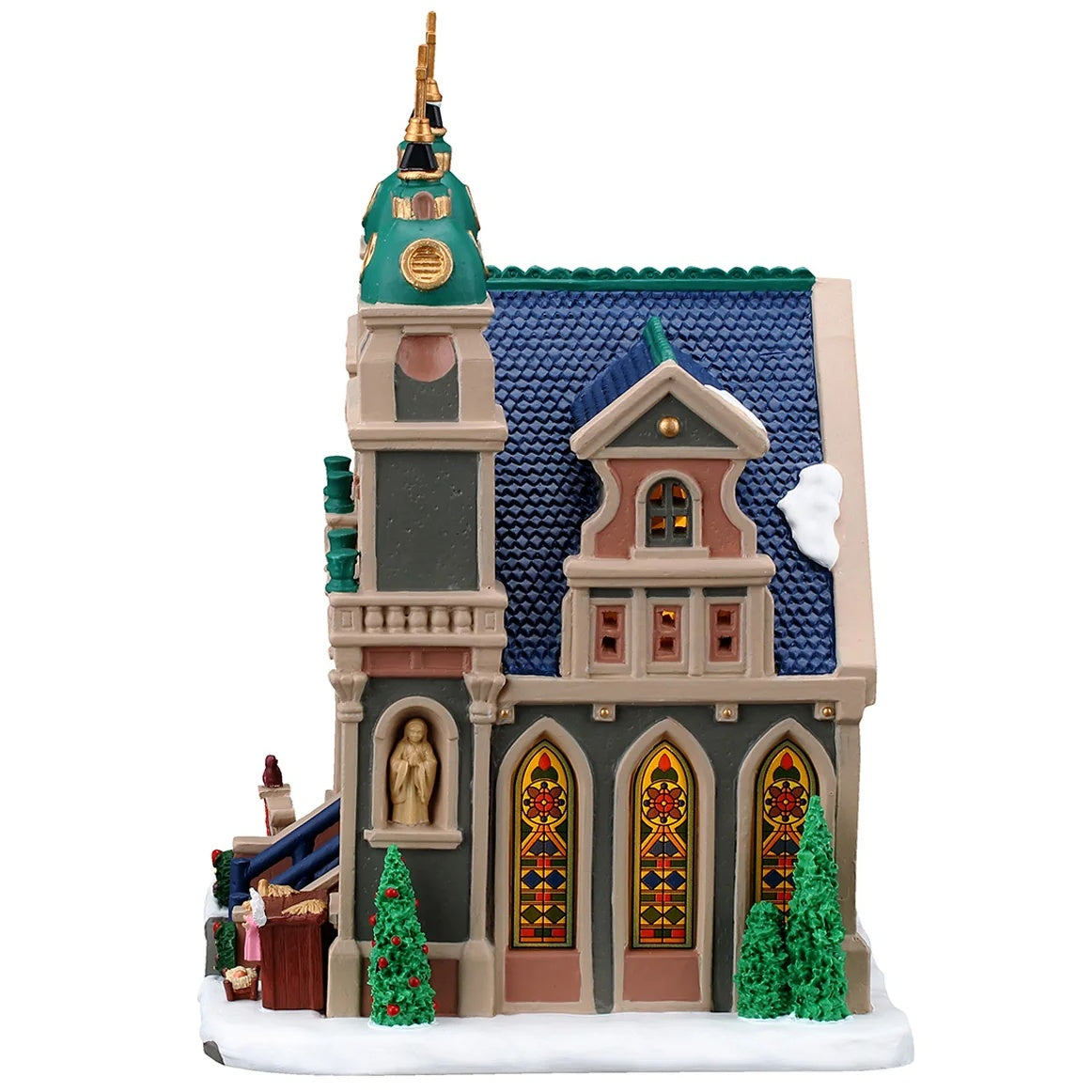 This image shows what the side of this building looks like. The roof is blue and there's a bit of snow. There are three stained glass windows. There's a statue of Mary and there are three tall trees.